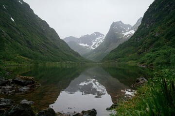 Wall Mural - Serene lake reflects mountains, in lush valley under overcast sky. Travel & nature