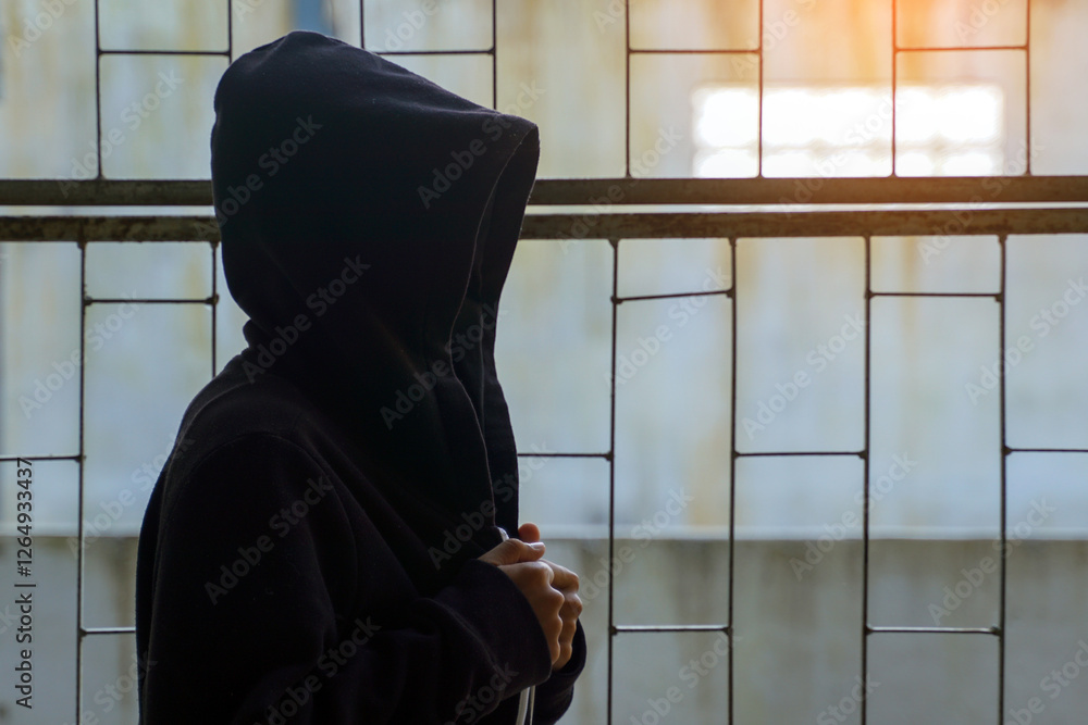Asian boy wearing a hoodie covering his face sits alone in a hidden ...