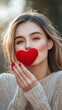 © Julia - A woman blows a kiss holding a red heart to her face