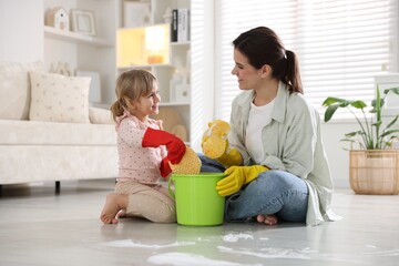 Wall Mural - Cute little girl helping her mother cleaning floor at home