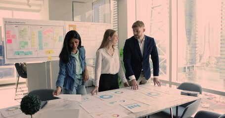 Wall Mural - Successful diverse team of positive young business colleagues working on startup strategy together, discussing marketing reports in meeting room, talking at table with paper graphs