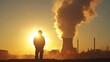 © atipong - A Worker Silhouetted Against a Majestic Sunset and Towering Power Station Plume