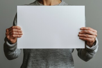 Poster - A man is shown holding a white blank poster in front of a grey background, captured in closeup, serving as a mockup for design purposes