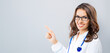 © vgstudio - Portrait image - happy smile female doctor, brunette haired woman wear eyeglasses, eye glasses, white coat show point finger, advertise at free space, empty blank ad area, isolate grey gray background
