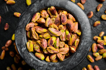 Wall Mural - Stone mortar with pistachio kernels, preparation of pistachio flour. Macro photo, close-up, on a black slate table.