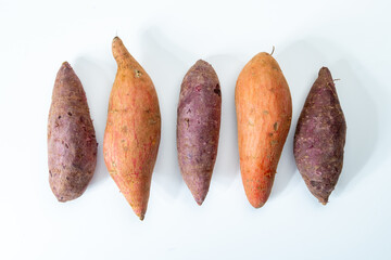 Wall Mural - Colorful sweet-tasting tuberous roots vegetables purple and orange organic sweet potatos close up