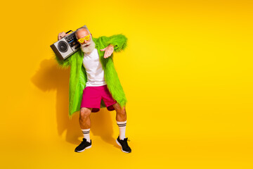 Canvas Print - Stylish elderly man with beard wearing colorful outfit standing against yellow background holding boombox