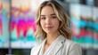 © renny - A young professional woman with blonde hair, wearing a white blouse and blazer, holding a digital wallet in front of a colorful financial chart on a screen.