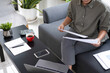 © MIND AND I - Businesswoman sitting at desk on couch in workplace or at home working on laptop and analyzing data on charts and graphs and writing on papers to make business plan and strategies for company