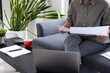 © MIND AND I - Businesswoman sitting at desk on couch in workplace or at home working on laptop and analyzing data on charts and graphs and writing on papers to make business plan and strategies for company