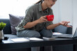 © MIND AND I - Businesswoman sitting at desk on couch in workplace or at home working on laptop and analyzing data on charts and graphs and writing on papers to make business plan and strategies for company