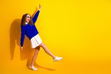 Wall Mural - Joyful young woman in stylish outfit celebrating and dancing against vibrant yellow backdrop