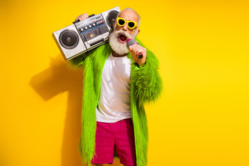 Canvas Print - Charismatic elderly man in eccentric attire holding a retro boombox against a vibrant yellow background