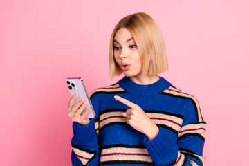 Wall Mural - Surprised Young Woman Interacting with Smartphone Against Pink Backdrop Wearing Blue Striped Pullover