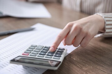 Budget. Woman with paperwork and calculator at wooden desk indoors, closeup