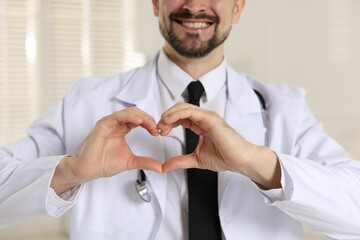 Wall Mural - Smiling cardiologist making heart with hands indoors, closeup