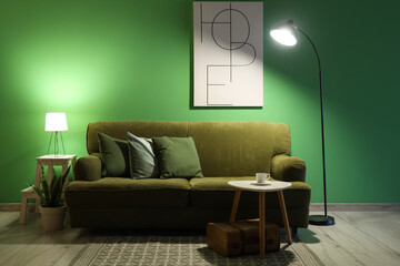 Wall Mural - Sofa, table with cup of coffee and glowing lamps in interior of living room