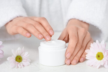 Wall Mural - Young woman with jar of cosmetic cream and chrysanthemum flowers on table against white background, closeup