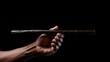 © Canities - Dark skinned Hand Holding a Long Dark Brown Wooden Stick Against Black Background