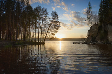 Wall Mural - The landscape, with its sunrise, reflects the surface of the water. Silhouettes of trees are visible on the rocky shore, at the exit of the bay.