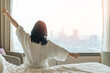 © Chinnapong - Hotel relaxation on lazy day with Asian woman take it easy, waking up from good sleep on bed in weekend morning resting in comfort bedroom city view having happy work-life quality balance lifestyle