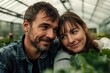 © Alla - A couple stands together in a lush greenhouse surrounded by plants and flowers