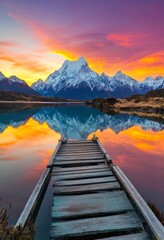 Wall Mural - The view at sunset, with snow-capped mountains reflected in the crystal clear water and an old wooden pier leading out into the calm water.