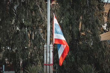 Thai flag half mast waves gently, solemn symbol of respect and remembrance against backdrop of lush greenery