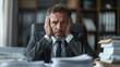 © zhia studio - Stressed businessman sitting at a cluttered desk surrounded by paperwork, depicting workplace pressure