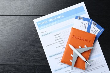 Sticker - Medical tourism. Travel insurance application form, passport with tickets and airplane model on black wooden background, top view. Space for text