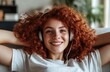 © thiquynh - A young woman with curly red hair is lying on the sofa at home, listening to music through headphones and smiling happily as she reads an e-book in her hand.