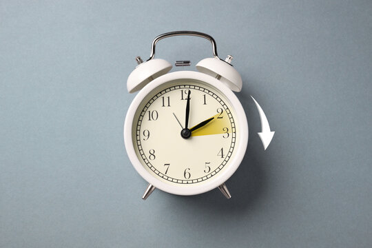 Wall Mural -  - daylight saving time. white alarm clock on grey background, top view. highlighted area and arrow sho