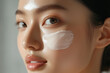 © Denis - Beautiful beauty Asian woman with skincare cream smear applied on her facial skin against pastel background. Cosmetic concept.