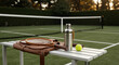 © Rizwan Akbar - A still life of tennis equipment, including a racket, balls, and a water bottle, conveying a sense of relaxed outdoor leisure, on a bench beside a tennis court
