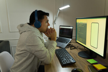 latin software developer wearing headphones concentrating on code displayed on computer monitor, wor