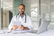 © Liubomir - Successful experienced doctor sitting at desk inside the clinic office and using a tablet computer. Man in a white medical coat, using an application for online communication and consulting patients.