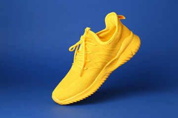 Wall Mural - Stylish yellow sneaker in air against blue background