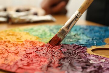 Wall Mural - Mixing paints on palette with brush at table, closeup