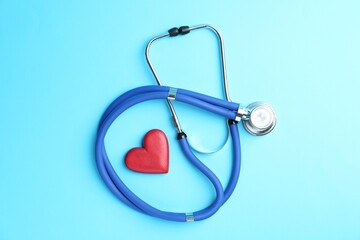 Wall Mural - Cardiology. Stethoscope and red decorative heart on light blue background, flat lay