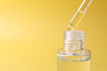 Wall Mural - Dripping serum from pipette into bottle on yellow background, closeup. Space for text