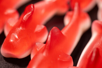 Wall Mural - A close-up of several red gummy shark candies with a white base arranged on a black surface. The candies have a shiny, translucent texture and a soft, chewy.