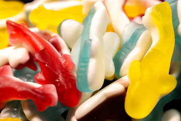 Wall Mural - A close-up of multi-colored gummy shark candies in red, yellow, blue and white. The candies have a shiny, translucent texture and are stacked together, creating a lively display.