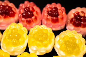 Wall Mural - Red and yellow gummy candies resembling raspberries and pineapples are arranged on a black background. The candies have a shiny, translucent texture.
