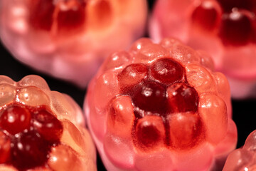 Wall Mural - A close-up of transparent raspberry-shaped gummy candies with a shiny, bumpy texture. The bright red and pink hues contrast against a dark background, highlighting their sweetness.