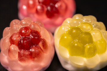 Wall Mural - Red and yellow gummy candies resembling raspberries and pineapples are arranged on a black background. The candies have a shiny, translucent texture.
