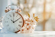 © vejaa - Spring forward. Time change in spring. Daylight saving time. Vintage alarm clock with melted snow, and tiny spring flowers. Clock turn forward one hour in spring
