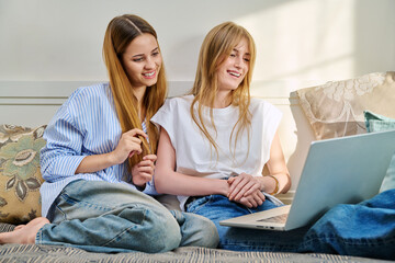 Wall Mural - Two young cheerful teenage girls friends students at home looking at laptop, sitting on couch