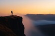 © BerkahStock - Silhouetted hiker on clifftop overlooking misty valley at sunrise.