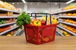 © Henhen - A red shopping basket filled with colorful peppers and leafy greens, placed on a wooden surface in a grocery store aisle.