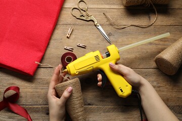 Wall Mural - Woman with hot glue gun making craft at wooden table, top view